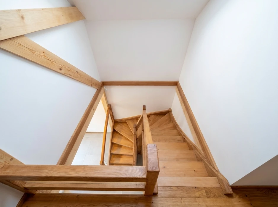 Escalier en bois massif clair photographié en plongée depuis l'étage supérieur