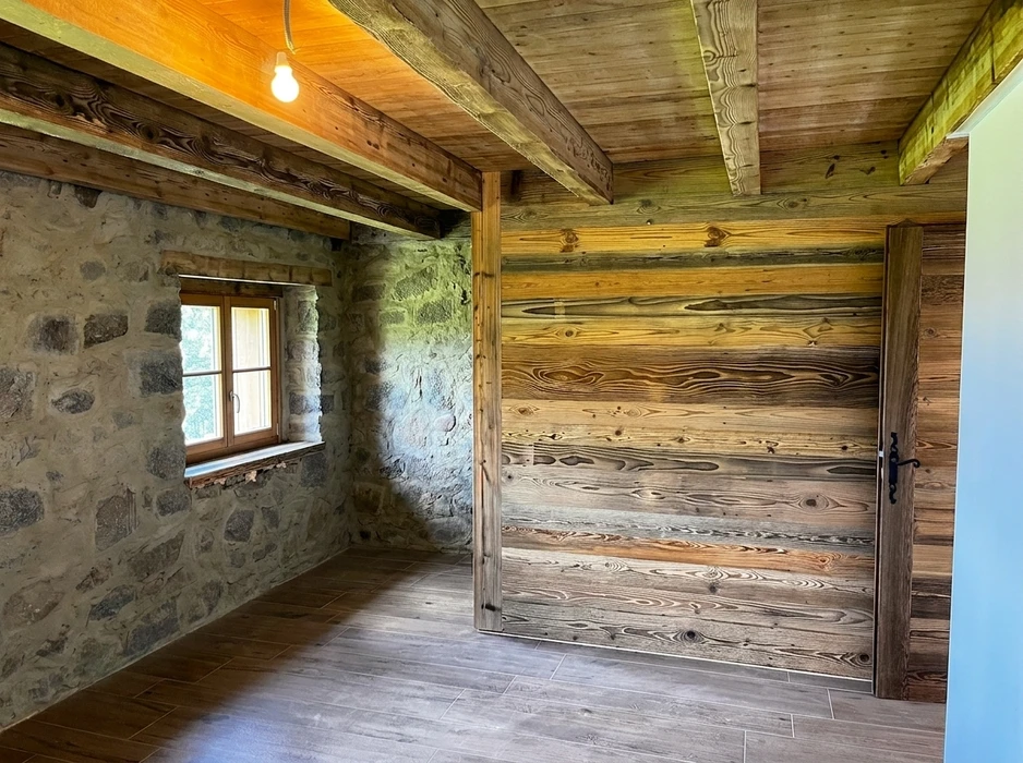 Intérieur rustique rénové combinant mur en pierre apparente irrégulière et cloison en planches de bois massif vieilli à grain prononcé