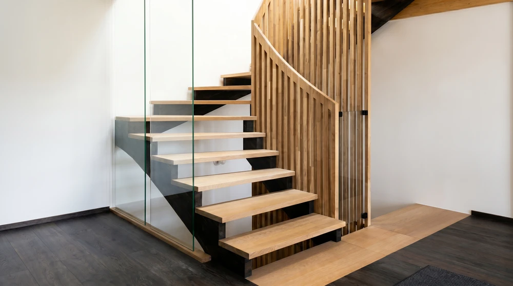 Escalier en bois massif vu de dessus, encadré d'une rambarde en verre trempé à joints noirs, menant à une cave en pierre apparente
