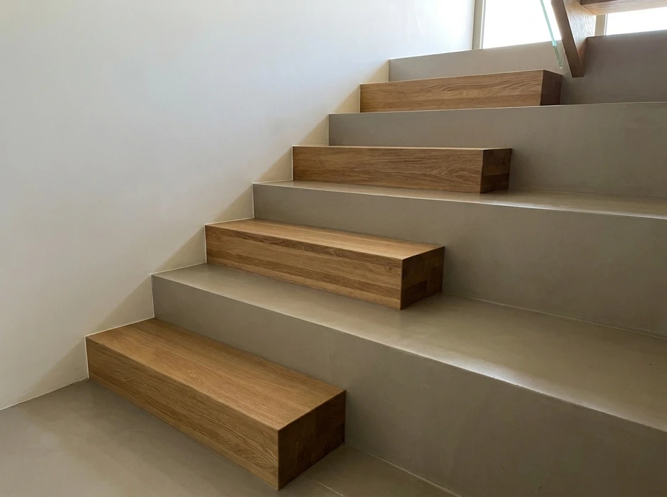 Escalier en bois massif vu de dessus, encadré d'une rambarde en verre trempé à joints noirs, menant à une cave en pierre apparente
