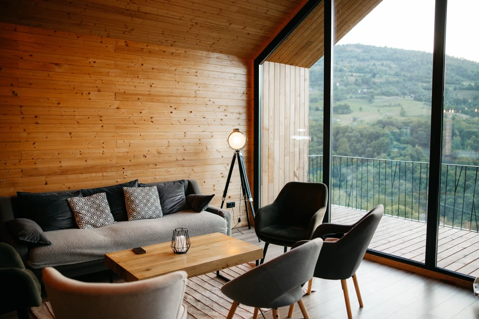 Salon moderne dans chalet montagnard avec mobilier contemporain gris, murs en rondins de bois brut, poutres apparentes au plafond